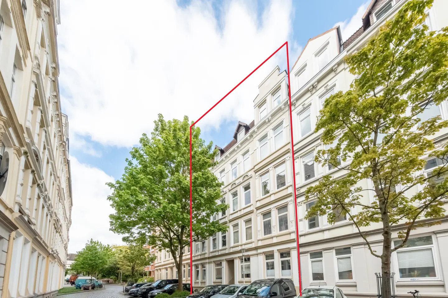 Exterior view of a multi-story white apartment building with a red outline, trees, and parked cars.