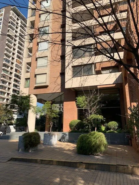 Exterior view of a tall brick apartment building with large windows and green landscaping.
