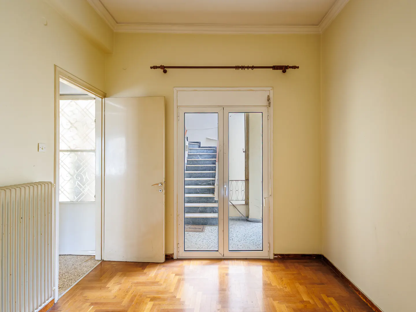 Empty room with yellow walls, herringbone wood floors, and glass doors opening to an outdoor staircase.