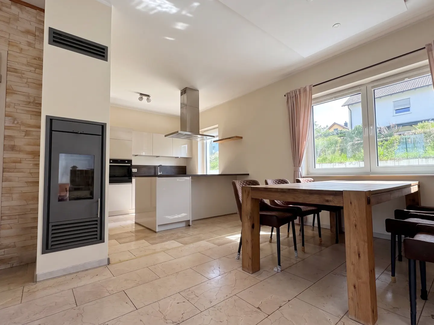 Open-concept kitchen and dining area with a fireplace, white cabinets, and a wooden table with brown chairs.