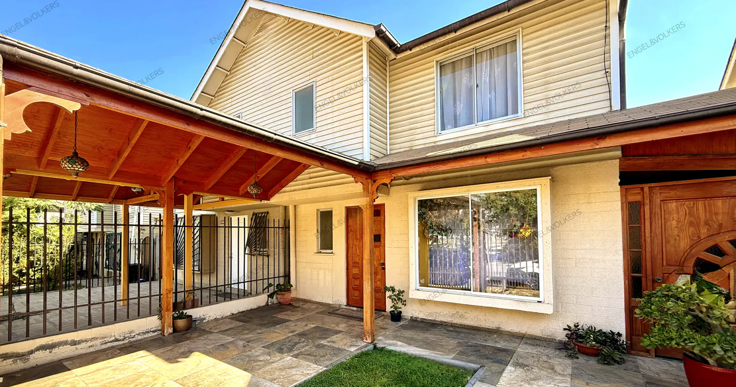 Two-story house with beige siding, a red-roofed porch, and a stone patio under a clear blue sky.