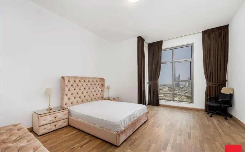 Bedroom with a tufted headboard bed, nightstands, lamps, and a large window with brown curtains overlooking a cityscape.