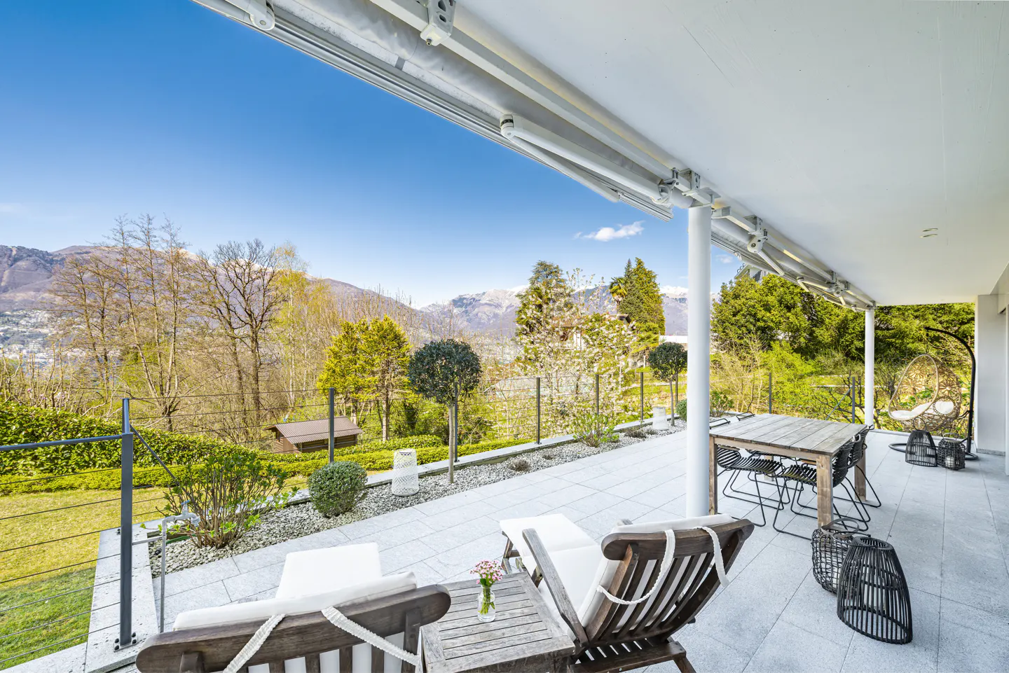 Covered patio with lounge chairs, dining table, and hanging chair. A mountain view is visible in the background.