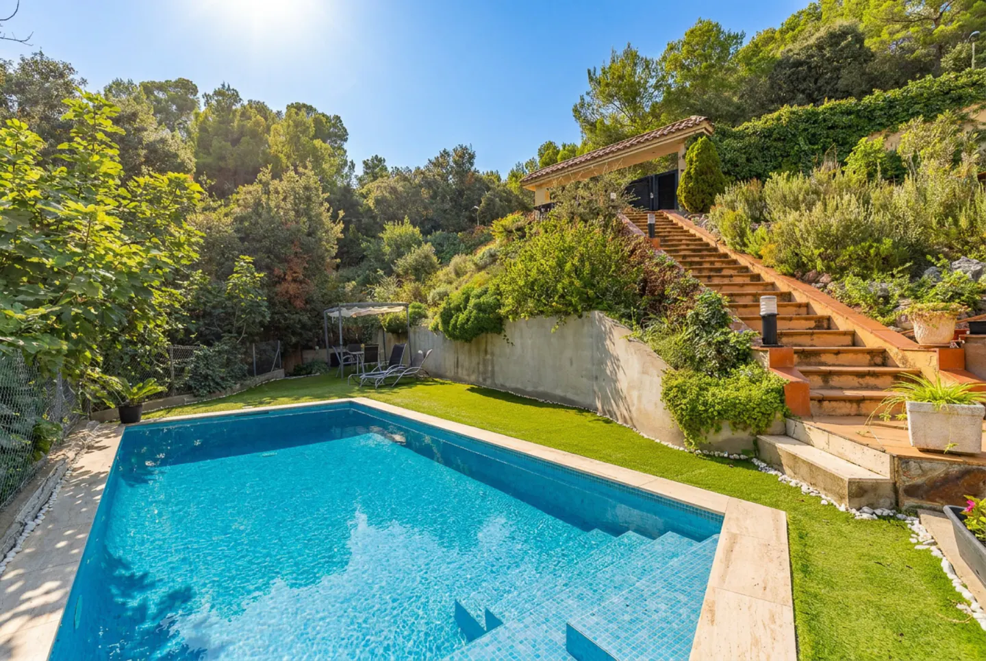 A backyard with a blue tiled pool, green grass, and a long staircase leading up a hill to a house.