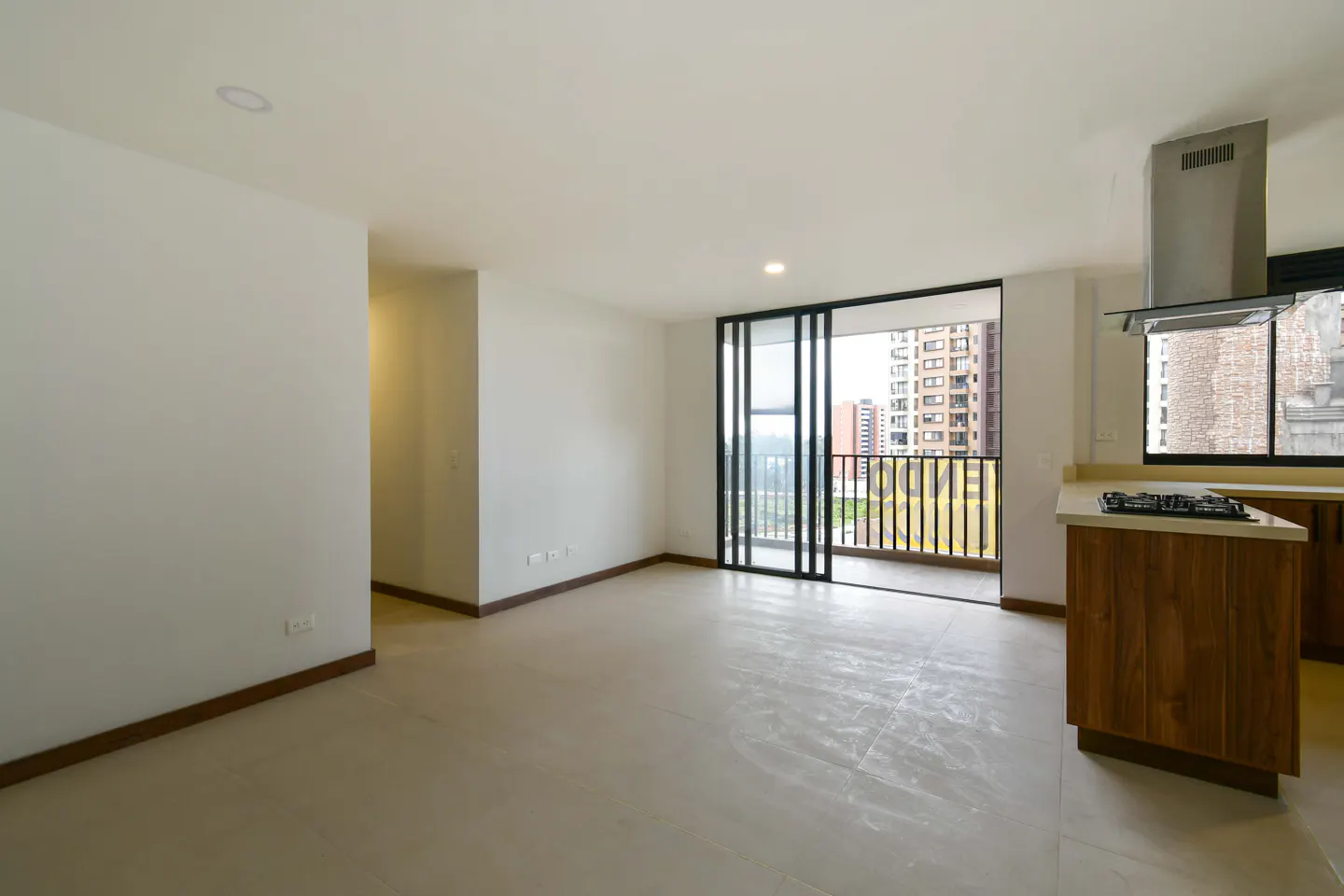 Modern open-plan apartment with white walls, light tile floors, a wooden kitchen island, and a balcony with city views.