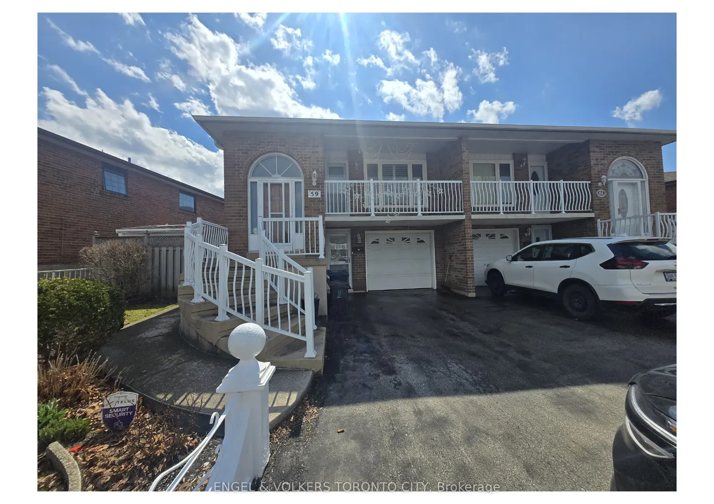 Two-story brick townhouse with white railings, arched doorways, and attached garages. A white SUV is parked in the driveway. Blue sky with clouds.
