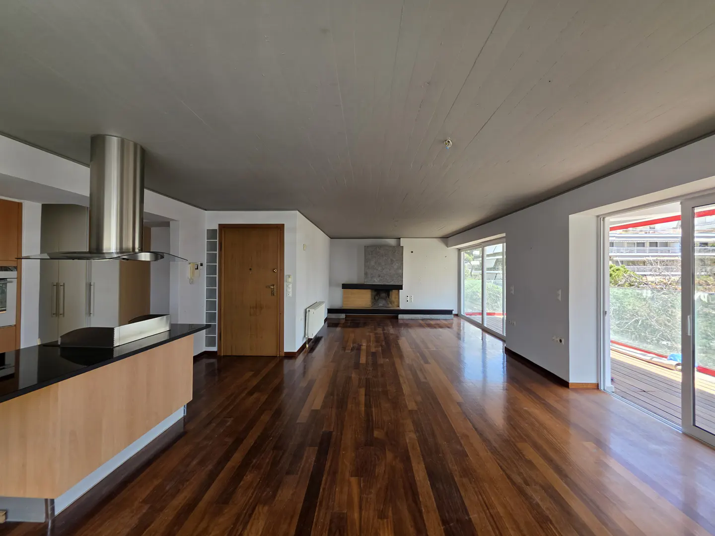 Open-concept living space with wood floors, a kitchen island, a fireplace, and sliding glass doors to a balcony.