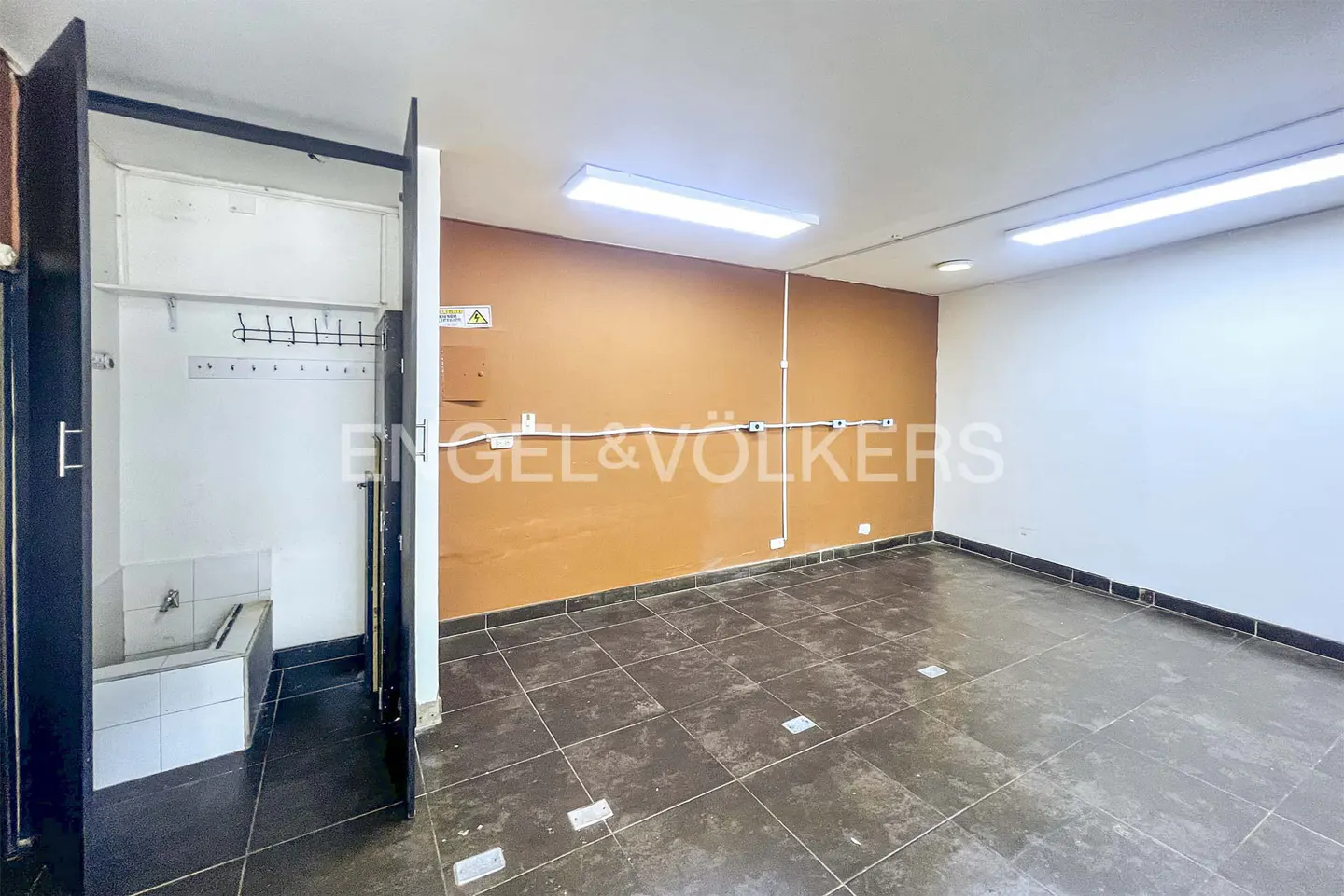 Empty room with brown tile floor, orange accent wall, and open closet with sink. Engel & Volkers logo visible.