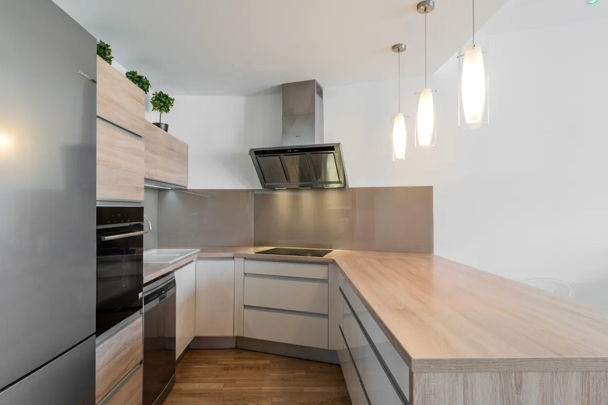 Bright kitchen with wood floors, white walls, and light wood cabinets. Stainless steel appliances and three pendant lights.