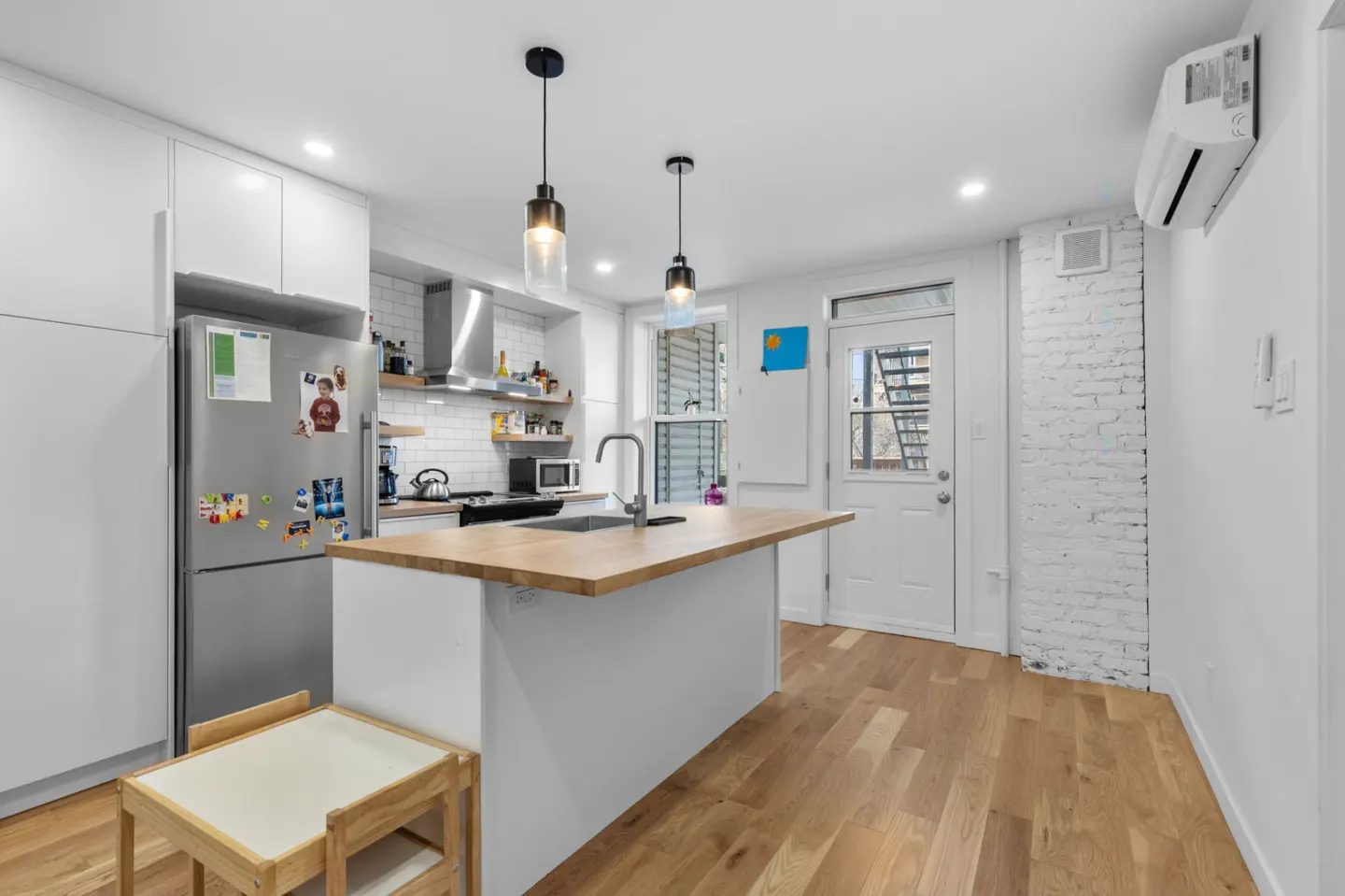 Bright kitchen with white cabinets, stainless steel fridge, and butcher block island. Hardwood floors and pendant lighting.