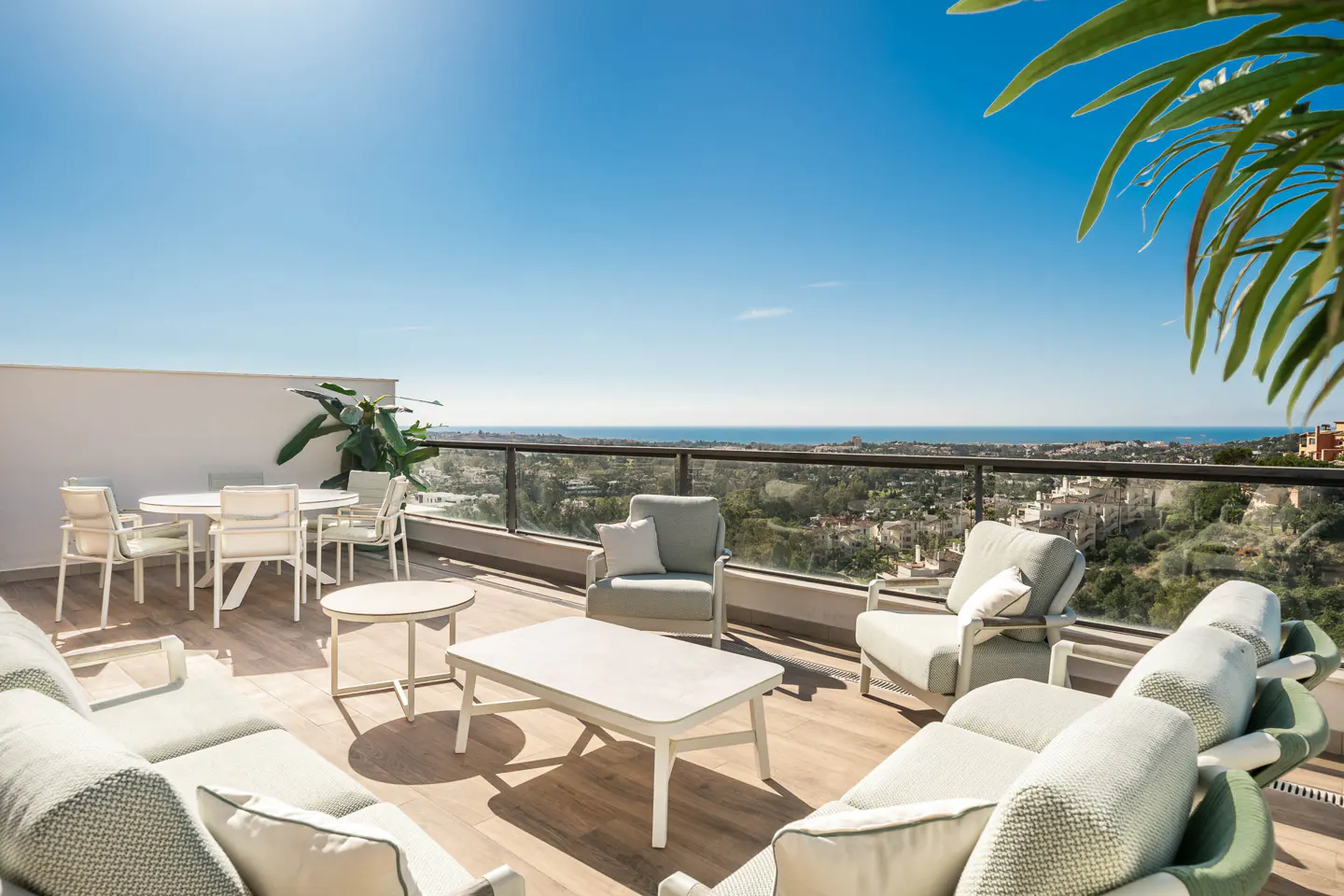 Outdoor patio with white furniture, including a dining set and lounge seating, overlooking a scenic view of the ocean and city.
