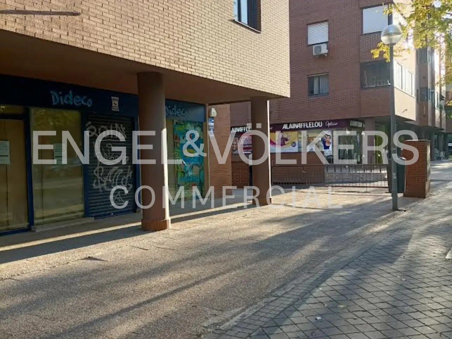 Commercial building with storefronts, including "Dideco" and "Alain Afflelou Opticien", under a brick building with pillars.