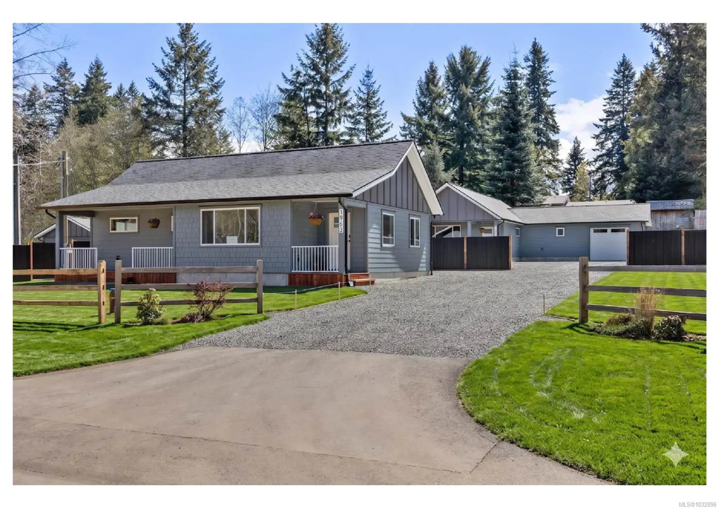 Exterior of a gray house with a gray roof, white trim, and a gravel driveway. Tall green trees are in the background.