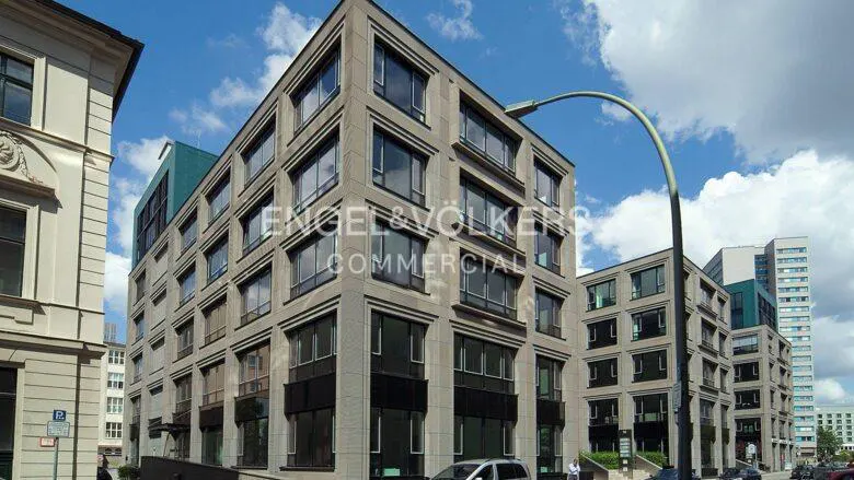 Exterior view of a modern, multi-story commercial building with large windows and a light gray facade under a partly cloudy sky.
