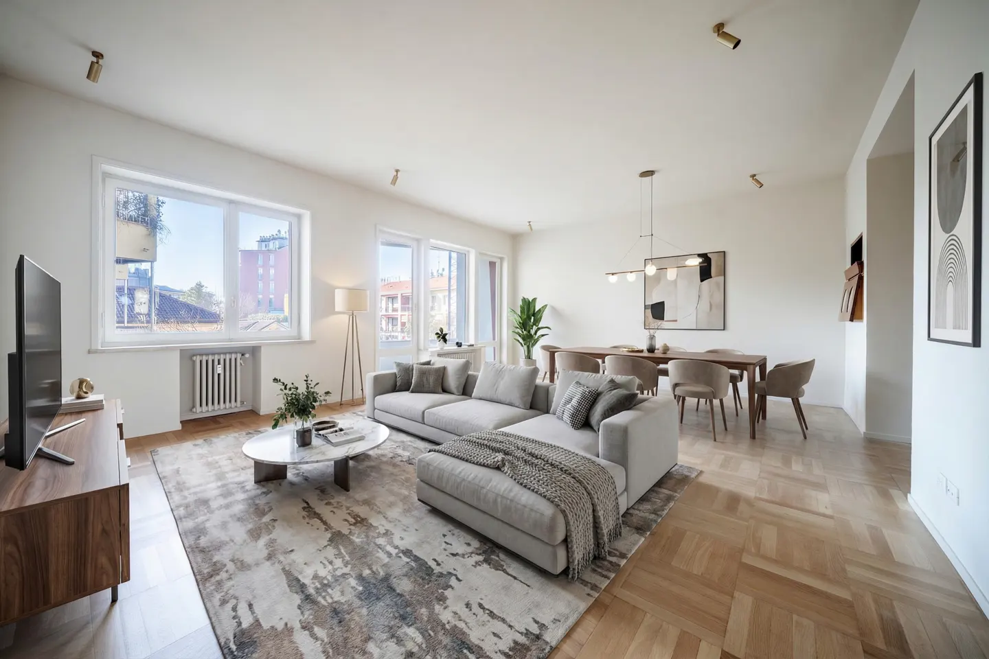 Bright, modern living room with a gray sectional sofa, marble coffee table, and wood dining table. Large windows offer city views.