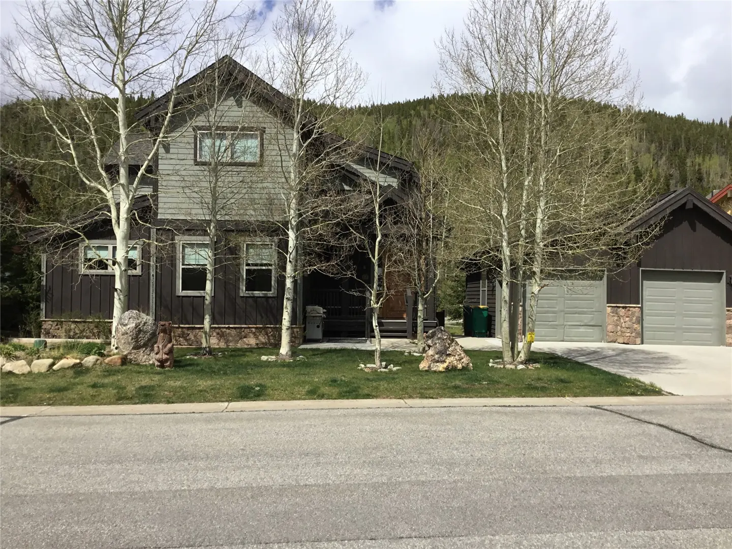Two-story house with brown siding and a gray garage. Trees line the front yard.