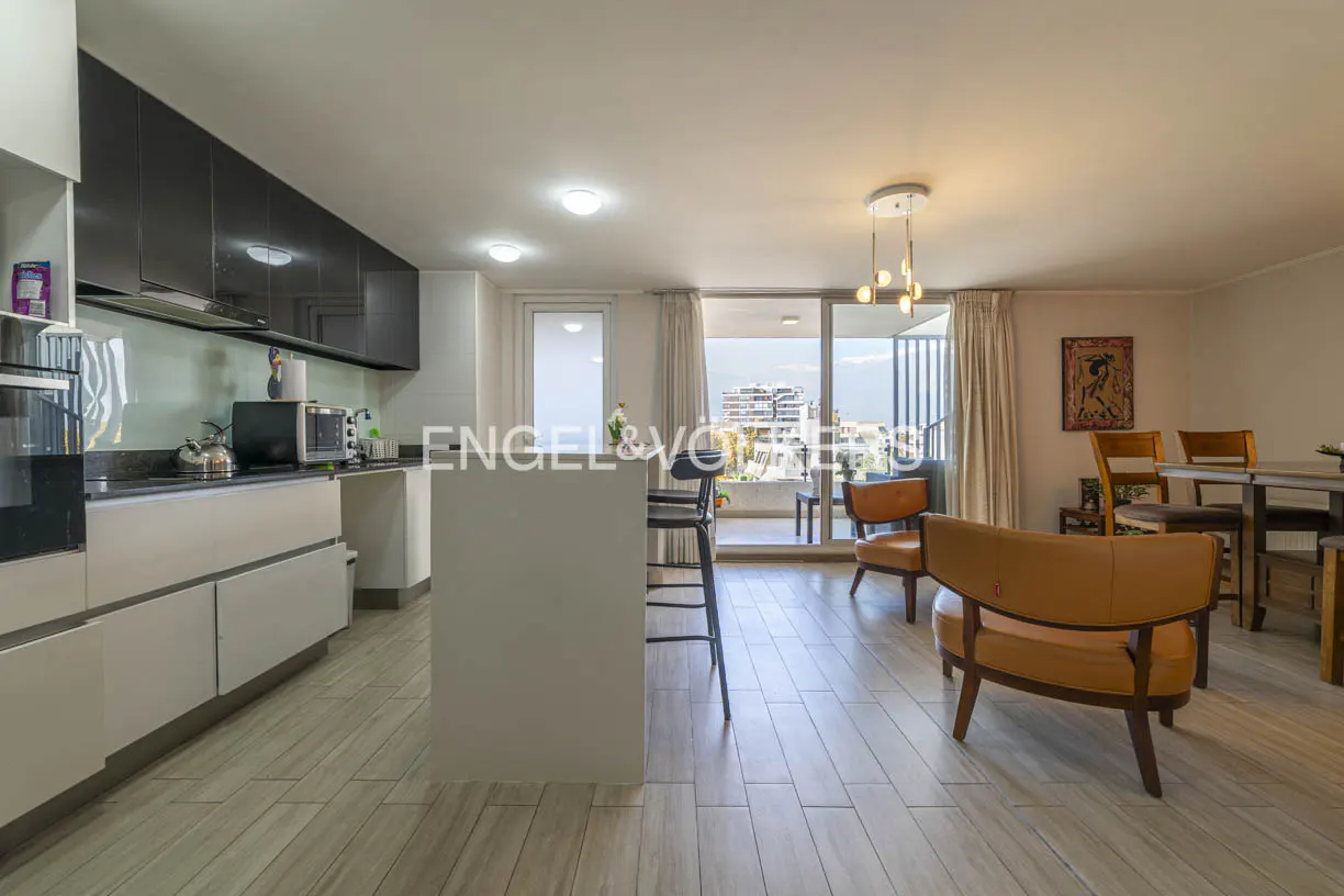 Open-concept apartment with a kitchen island, tan chairs, and a balcony with a city view.