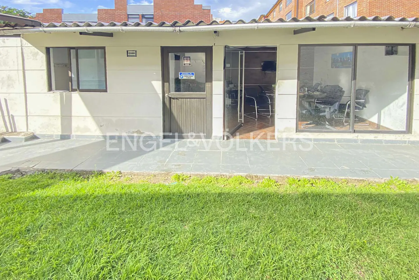 Exterior view of a one-story office building with a gray door and window, and a sliding glass door, with green grass in front.