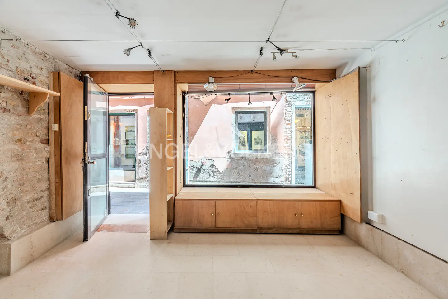 Interior view of a retail space with exposed brick, wooden fixtures, and a large window overlooking a narrow street.