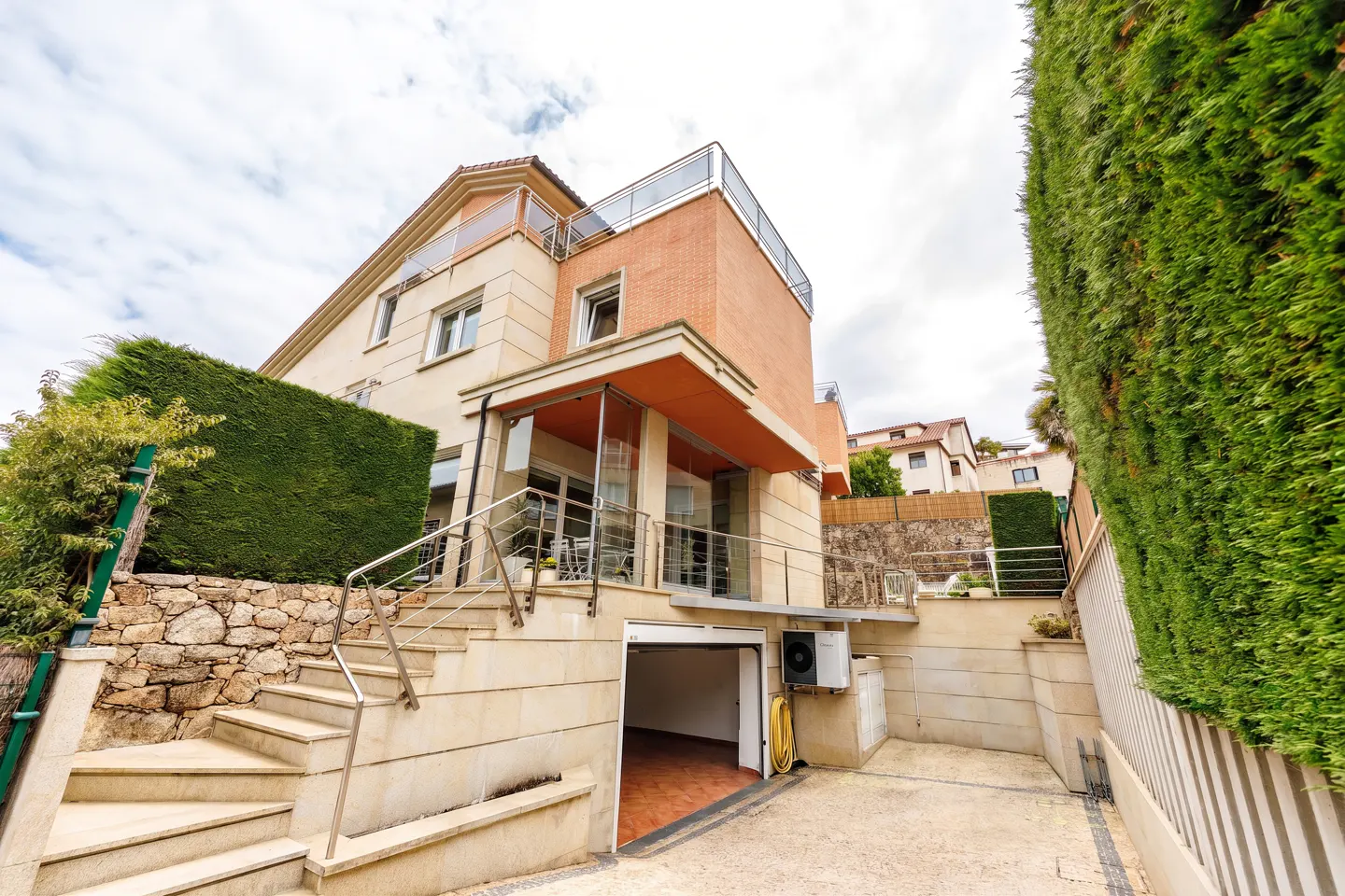 Exterior view of a modern two-story house with a garage, stone stairs, and green hedges.