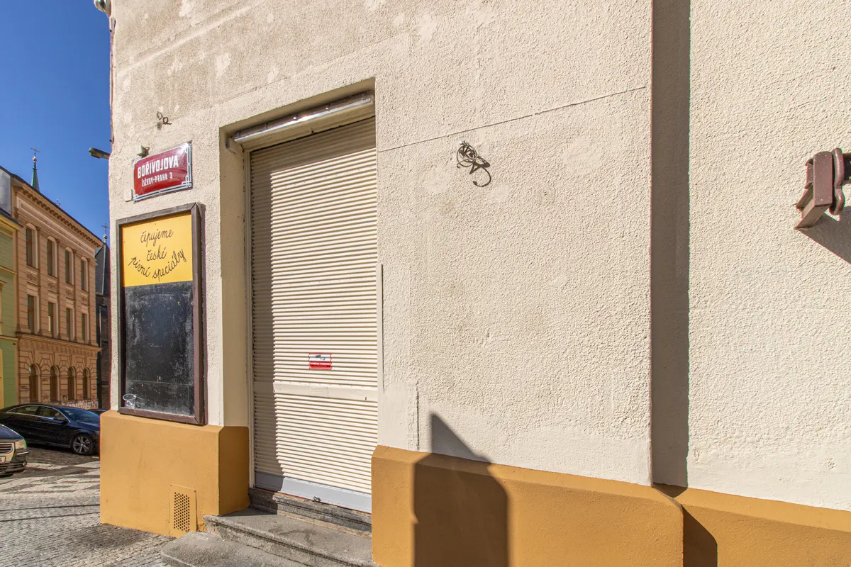 Exterior view of a building with a closed metal shutter door, a street sign, and a menu board.