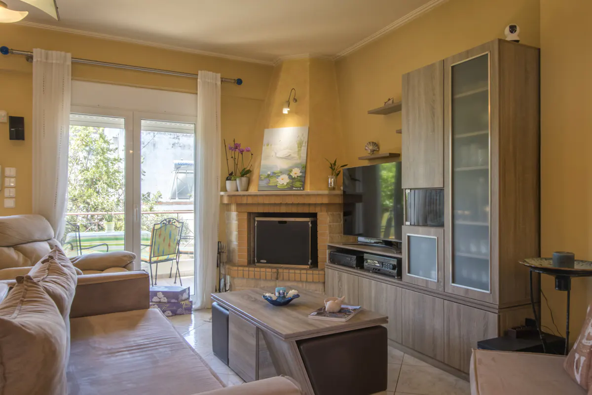 Cozy living room with a corner fireplace, wood media unit, TV, coffee table, and sliding glass doors to a balcony.