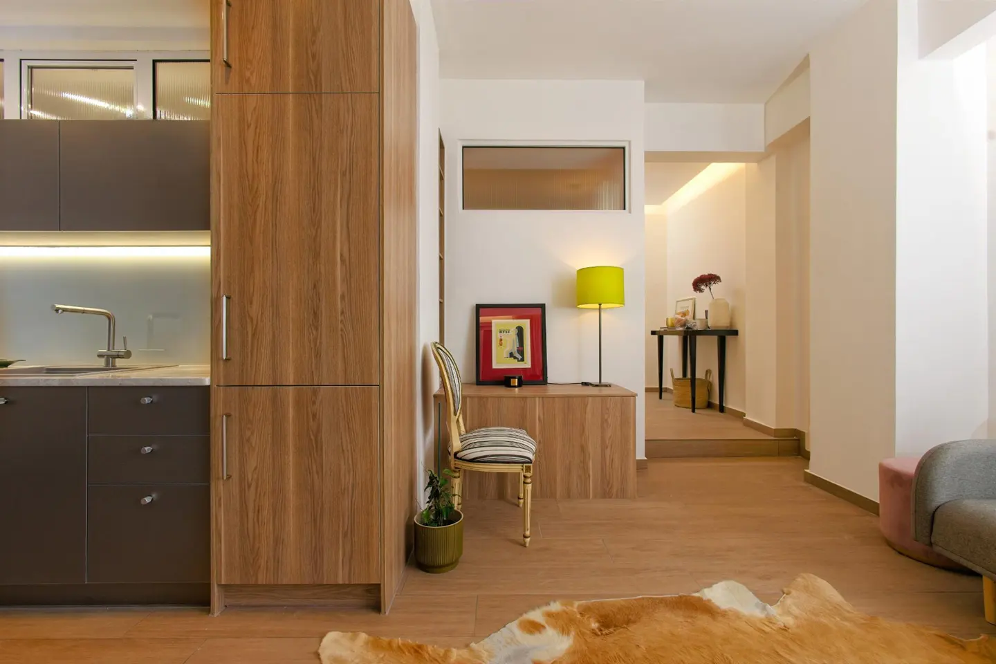 Modern kitchen with wood cabinets, a striped chair, a bright yellow lamp, and a cowhide rug on a light wood floor.