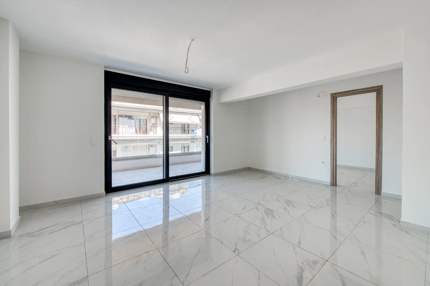Bright, empty room with white walls, marble tile floor, black-framed sliding glass doors to a balcony, and a doorway.