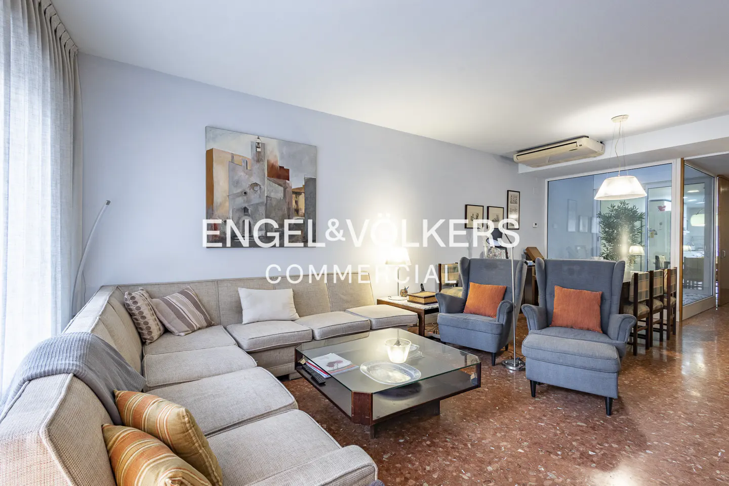 Living room with a large sectional sofa, two blue armchairs with orange pillows, and a glass coffee table.