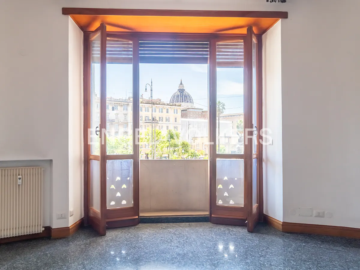 Interior view of a room with open wooden doors leading to a balcony with a city view.