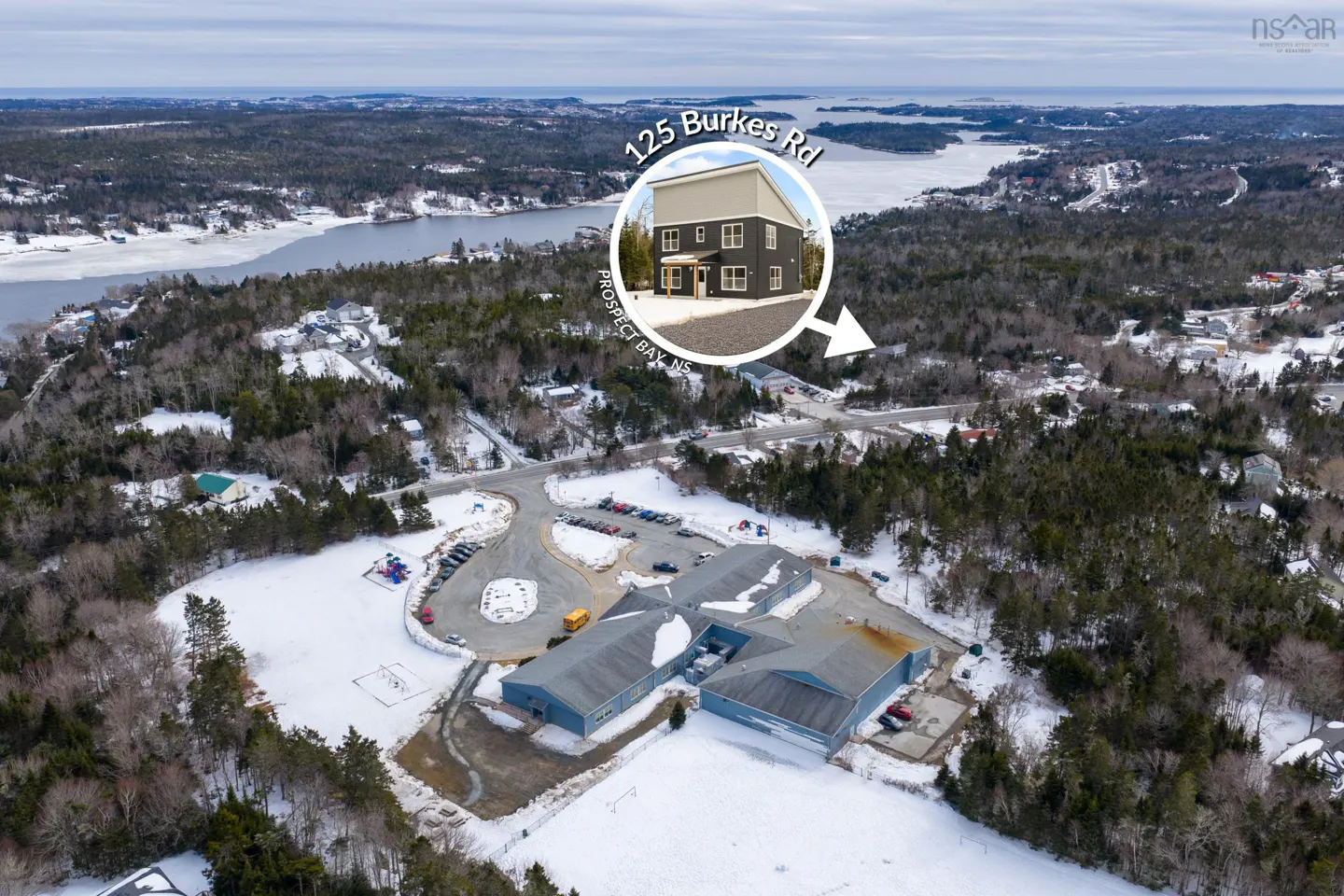 Aerial view of 125 Burkes Rd, Prospect Bay, NS, a two-story gray house, surrounded by snow-covered trees and a lake.