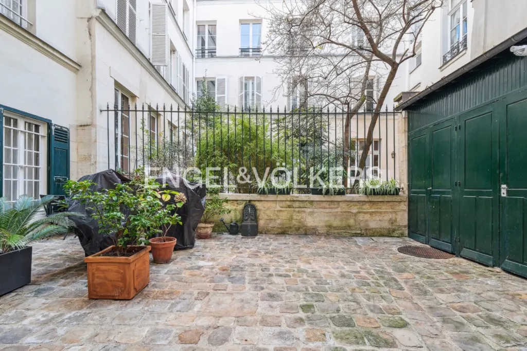 A cobblestone courtyard in Paris with potted plants, a black metal fence, and a dark green wooden garage door.