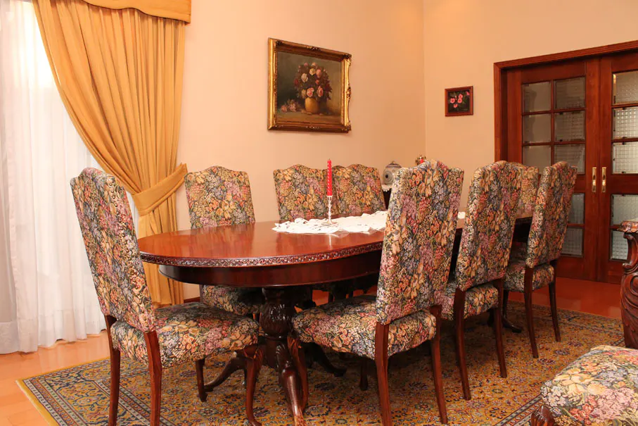 Formal dining room with a dark wood table, floral upholstered chairs, and gold curtains. A painting hangs on the wall.