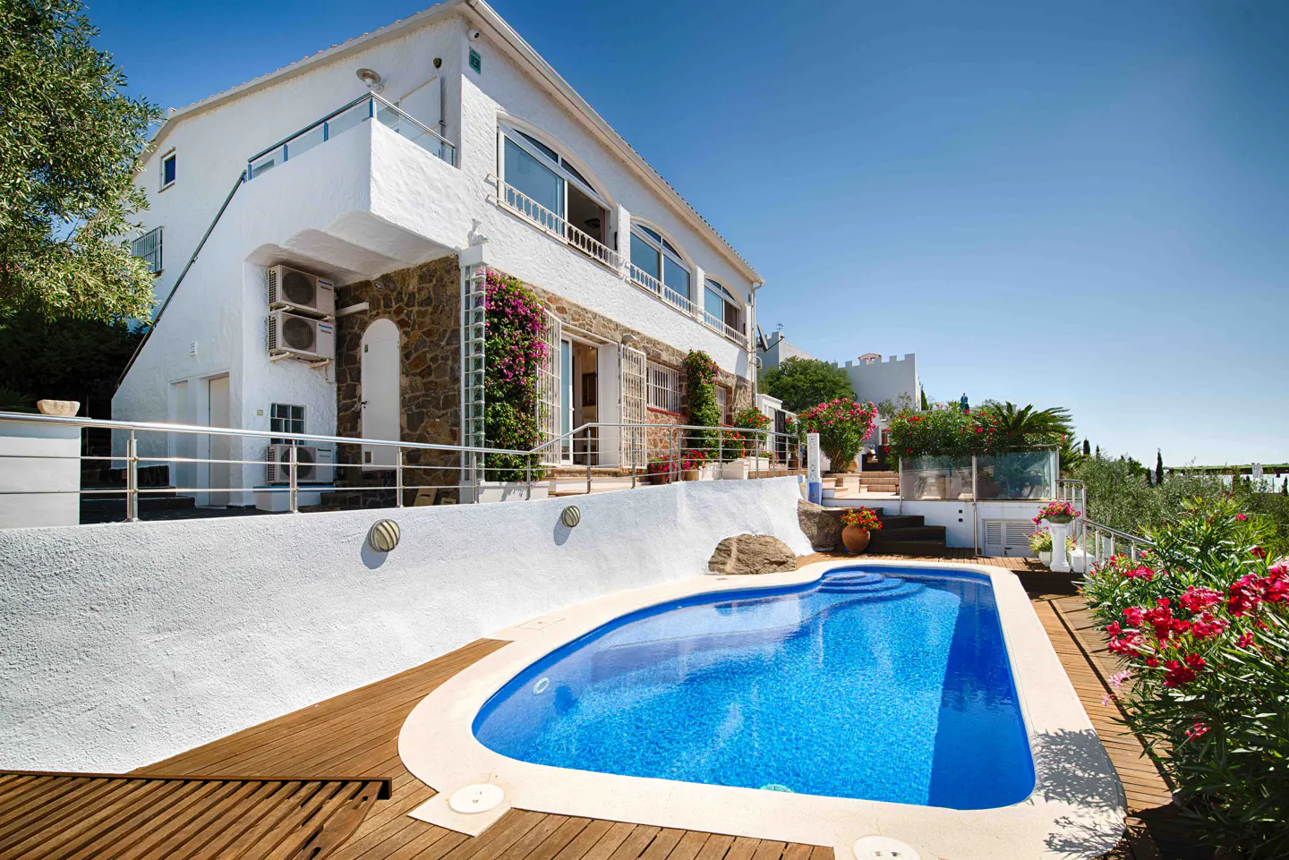 Exterior view of a two-story white house with a blue pool and wooden deck under a clear blue sky.