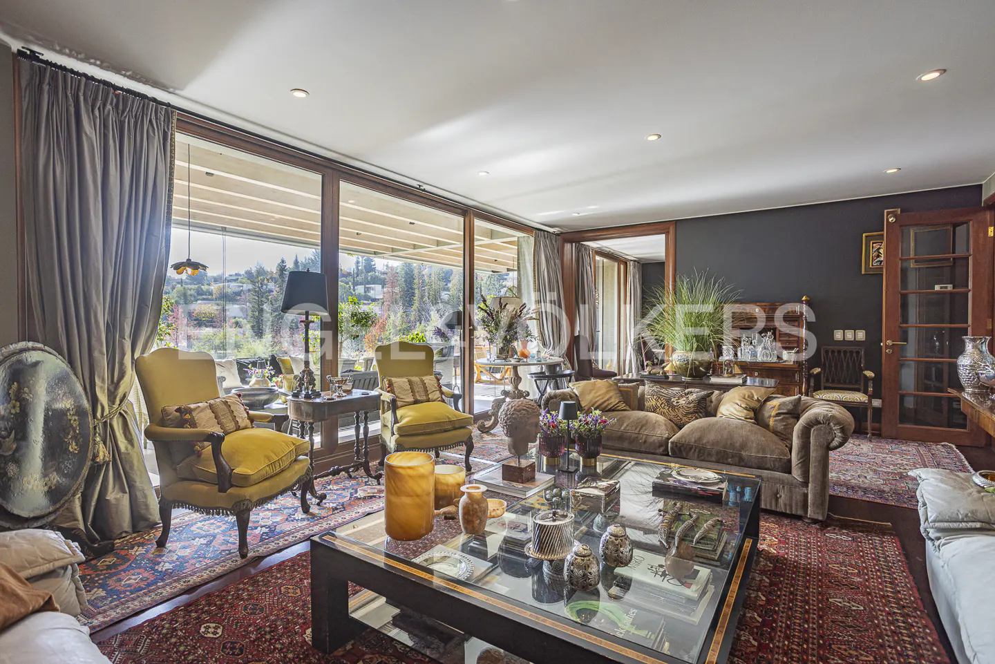 Living room with two yellow armchairs, a brown sofa, glass coffee table, and large windows overlooking a garden.