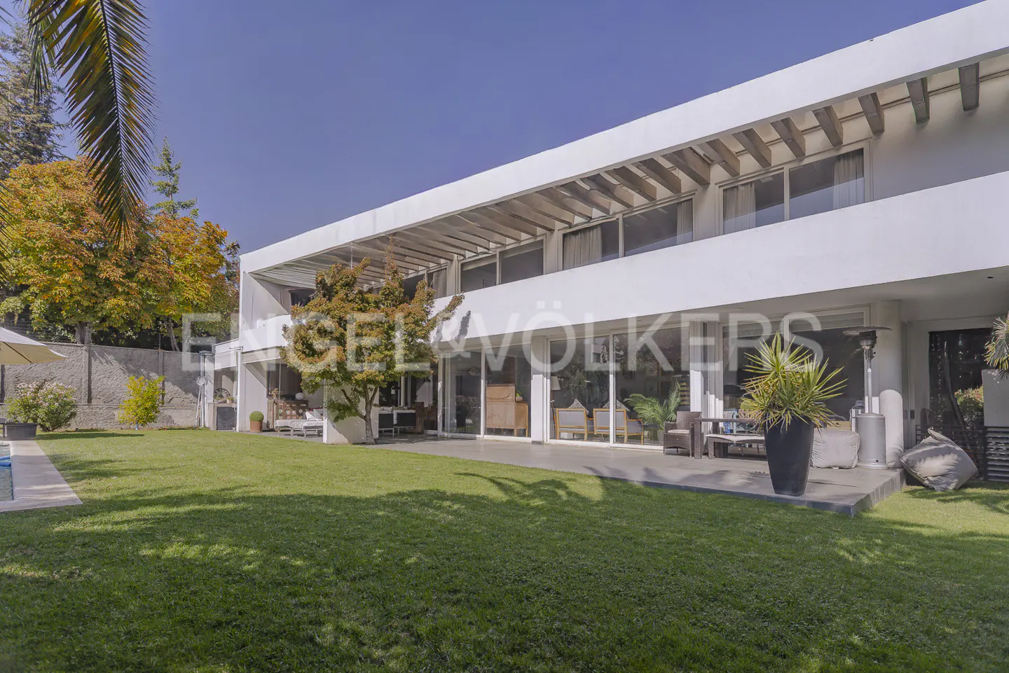 Two-story modern white house with a large green lawn and trees under a blue sky.