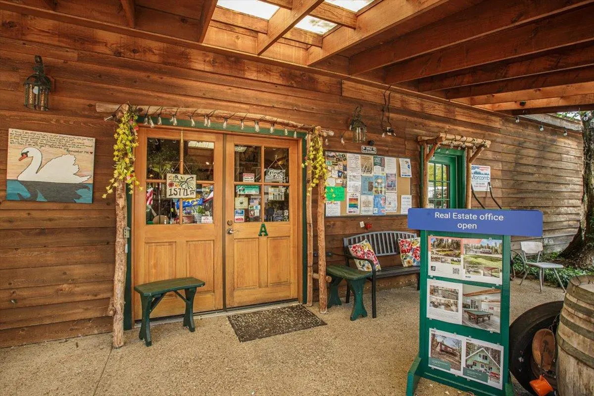 Rustic wooden real estate office entrance with double doors, a bench, a bulletin board, and an open sign on a stand.