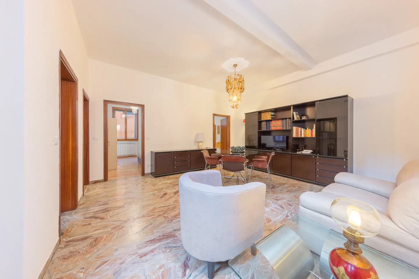 A living room with marble floors, a white sofa, a glass table, and a brown cabinet with a TV and books.