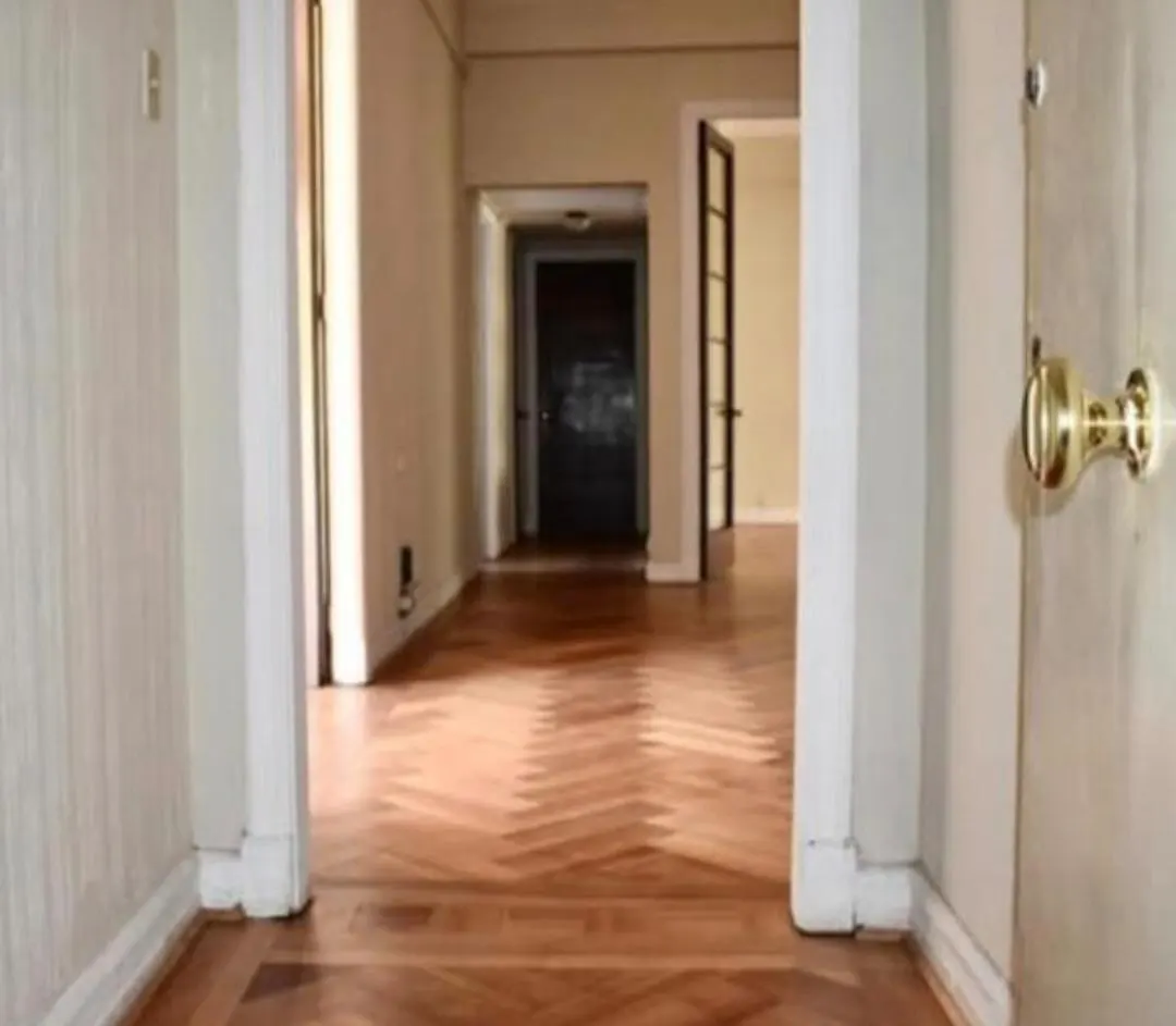 Hallway view with herringbone wood floors, white walls, and doorways leading to other rooms. A brass doorknob is visible on the right.