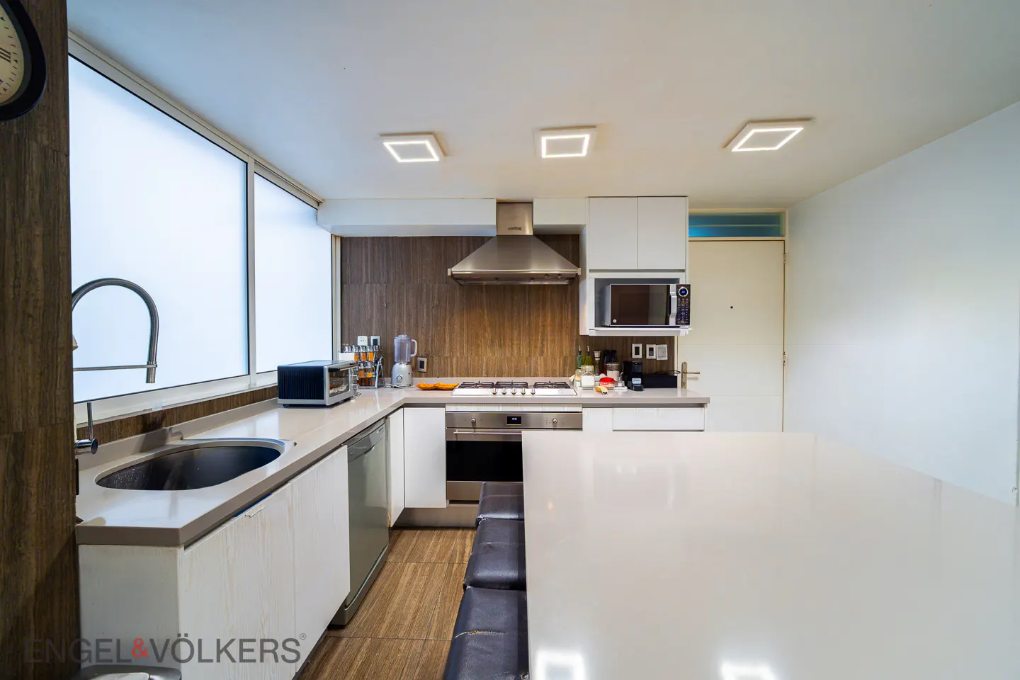 Modern kitchen with white cabinets, wood-paneled backsplash, stainless steel appliances, and a large white island with stools.