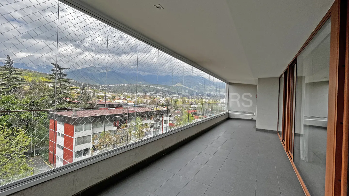 A long balcony with a wire fence overlooks a city with mountains in the background.