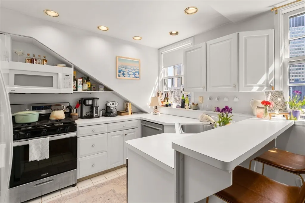 Bright, white kitchen with stainless steel appliances, a breakfast bar with two stools, and a window with city views.