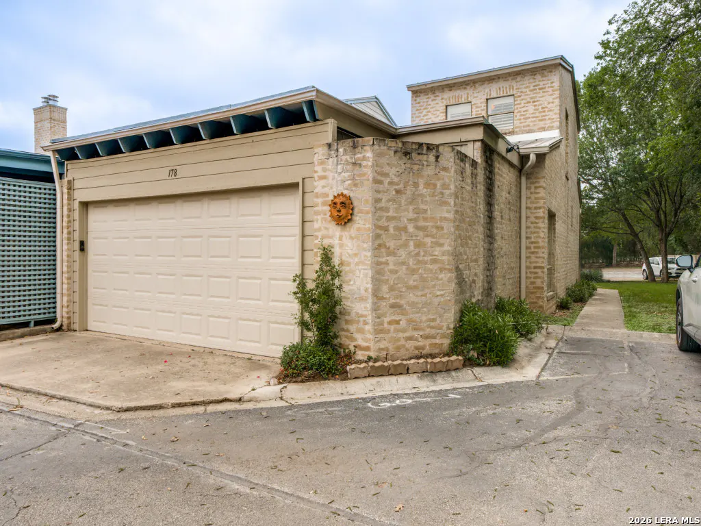 Exterior view of a beige house with a white garage door and a brick wall with a sun decoration.