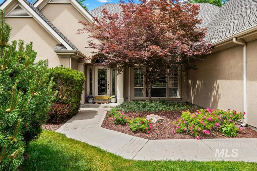 Front view of a beige house with a red tree, green bushes, and a concrete walkway leading to the front door.