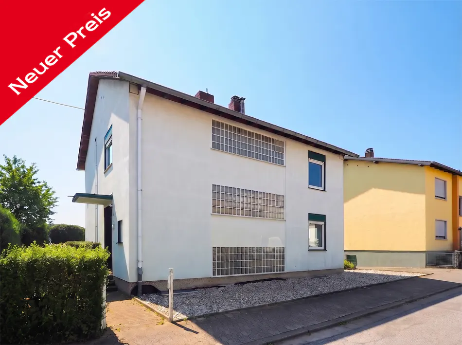 Two-story white house with a red "Neuer Preis" banner in the upper left corner. The house has multiple windows and a small front yard.