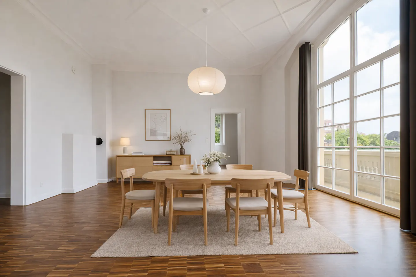Bright dining room with wood floors, oval table, six chairs, and large windows with a balcony view. A white pendant light hangs above.