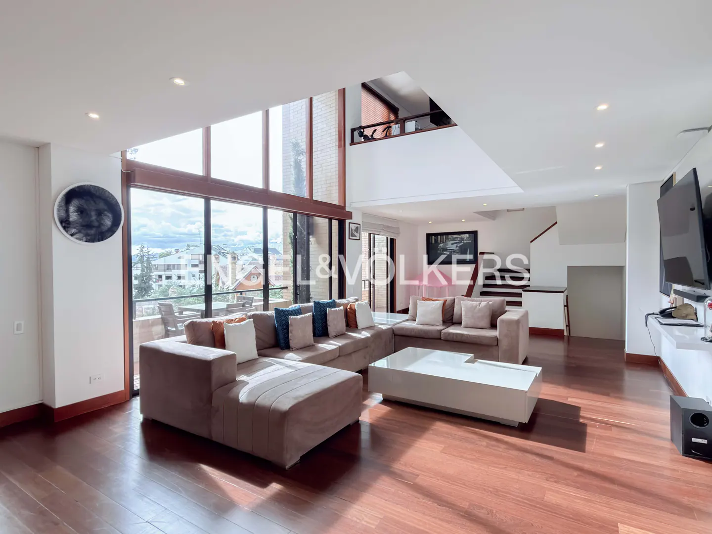 Spacious modern living room with large windows, a beige sectional sofa, white coffee table, and dark hardwood floors.