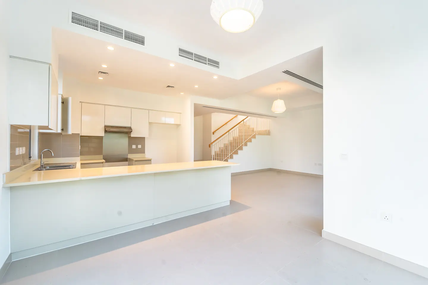 Bright, modern kitchen and living area with white cabinets, island, and staircase.
