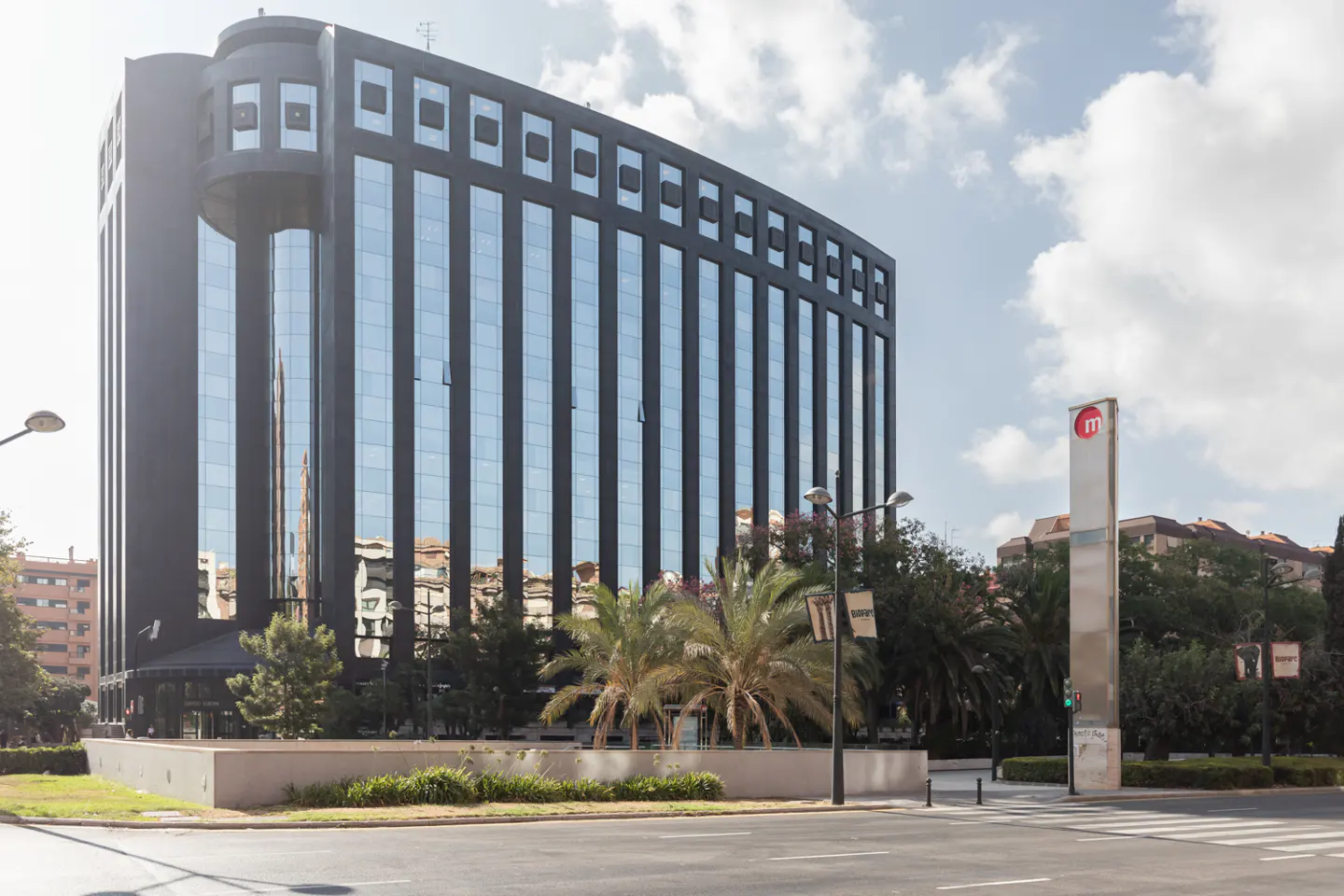 Exterior view of a modern, black office building with reflective glass windows, near a metro station entrance.