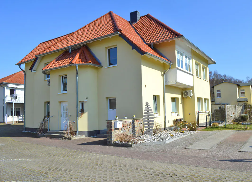 Two-story yellow house with a red tile roof and white trim on a sunny day.